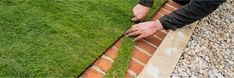 a man is cutting grass on the side of a brick wall