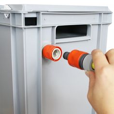 a hand is holding a screwdriver near a gray box with an orange door