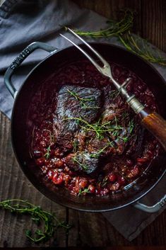 a pot filled with meat and garnish on top of a wooden table next to a knife