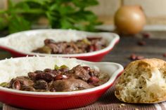 two red bowls filled with meat and rice next to bread on a wooden table top