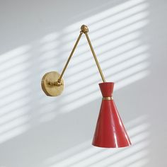 a red lamp hanging from the side of a wall next to a white wall with shadows on it