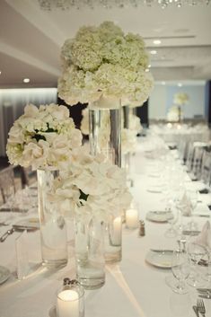 white flowers are in tall vases on the table at a wedding reception with candles and place settings