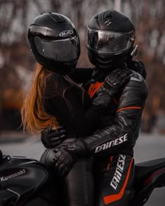 two people on a motorcycle wearing helmets and protective gear, one is hugging the other