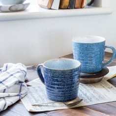 two blue coffee cups sitting on top of a wooden table next to an open book