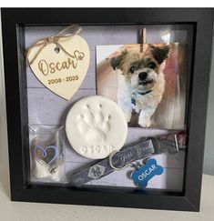 a dog's paw print is displayed in a shadow box with two tags and a heart shaped ornament