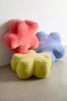 three different colored pillows sitting next to each other on the floor in front of a white wall