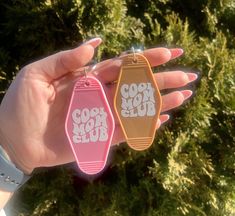 two pink and brown tags with the words cool mom club on them in front of some trees