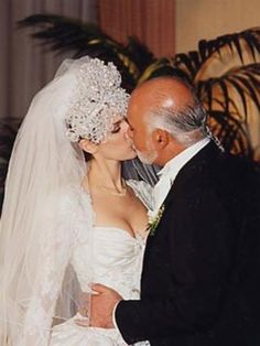 an older man and woman kissing each other in front of a wedding cake with white frosting on it