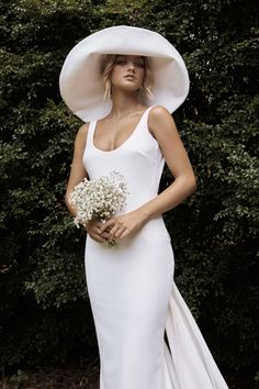 a woman in a white dress and large hat holding a bouquet of baby's breath flowers