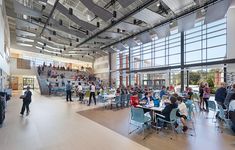 people are sitting at tables in a large room with high ceilings and lots of windows