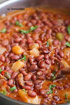 a pot filled with beans and vegetables next to a wooden spoon