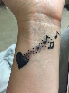 a small wrist tattoo with musical notes and a black heart on the left side of the wrist