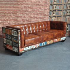 a leather couch sitting in front of a brick wall with lots of license plates on it