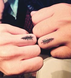 two people holding hands with tattoos on their fingers and one has a fishbone tattoo