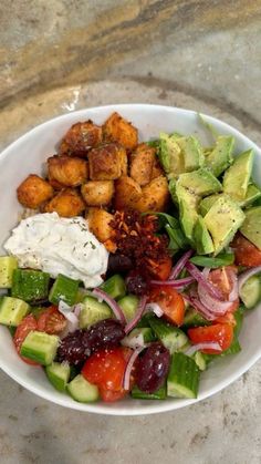 a white bowl filled with lots of food on top of a marble counter next to a knife and fork