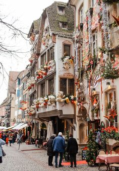 people are walking down the cobblestone street in an old european town with many decorated buildings