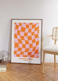 an orange and pink poster sitting on top of a wooden floor next to a chair