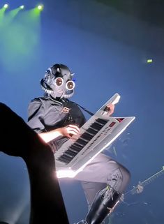 a man in a gas mask playing an electronic keyboard on stage with lights behind him