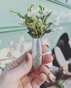 a person holding a silver spoon with flowers in it