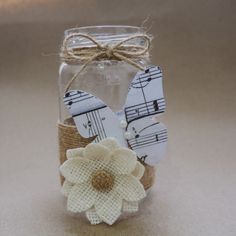 a glass jar filled with musical notes and a white flower on top of twine