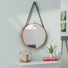 a mirror hanging on the wall next to a shelf with a candle and potted plant