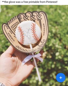 a hand holding a baseball lollipop with a ribbon around it's end