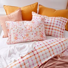 an unmade bed with orange and pink pillows