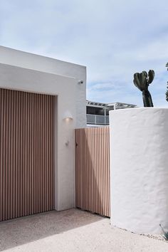 a white building with a cactus in the corner and a wooden fence on the other side