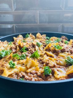 a skillet filled with pasta and cheese on top of a counter next to a brick wall