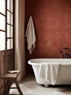 a white bath tub sitting in a bathroom next to a wooden door and window with red walls