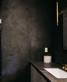 a bathroom with black walls and marble counter tops, along with a gold faucet