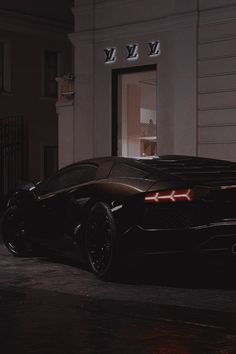 a black sports car parked in front of a building at night with its lights on