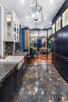 a large kitchen with marble counter tops and blue cabinetry, along with a chandelier hanging from the ceiling