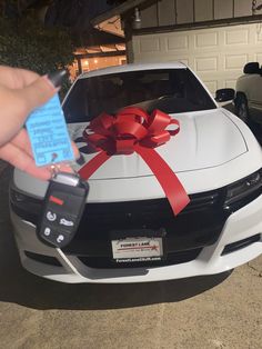 a hand holding a car key with a red bow on it and a tag attached to the hood