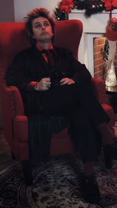 a man sitting in a red chair next to a christmas tree