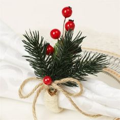 a pine branch with red berries tied to it on top of a white table cloth