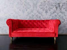 a red couch sitting on top of a hard wood floor next to a white wall