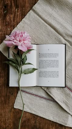 an open book with a pink flower on top of it next to a folded piece of cloth