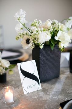 the table is set with white flowers in black vases and place cards on it