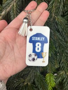 a hand holding a keychain with a soccer jersey on it and a trophy