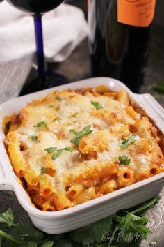 a casserole dish with cheese and parsley next to a bottle of wine