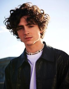 a young man with curly hair wearing a leather jacket