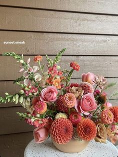 a vase filled with lots of flowers sitting on top of a white table next to a wooden wall