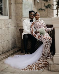 a bride and groom sitting on a bench in front of a building