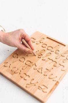 a person is writing on a wooden board with numbers and letters carved into the wood