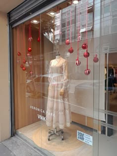 a mannequin in a window with red ornaments hanging from it's sides