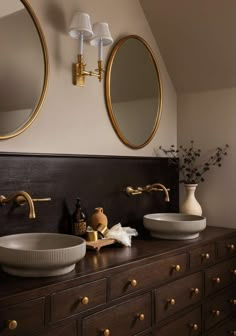 two bathroom sinks with gold faucets and round mirrors above them, on a dark wood dresser