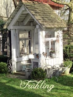 a small white shed sitting on top of a lush green field next to a tree