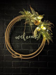 a wreath with lights hanging on the side of a brick wall that says welcome in front of it