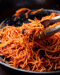 a pan filled with shredded carrots on top of a wooden table next to a fork